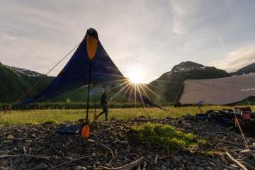 Two kitchen tarps set up with kayak paddles supporting them on a rocky beach with driftwood