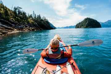 A child sits in the front seat of a double sea kayak in Resurrection Bay on a private family kayak tour