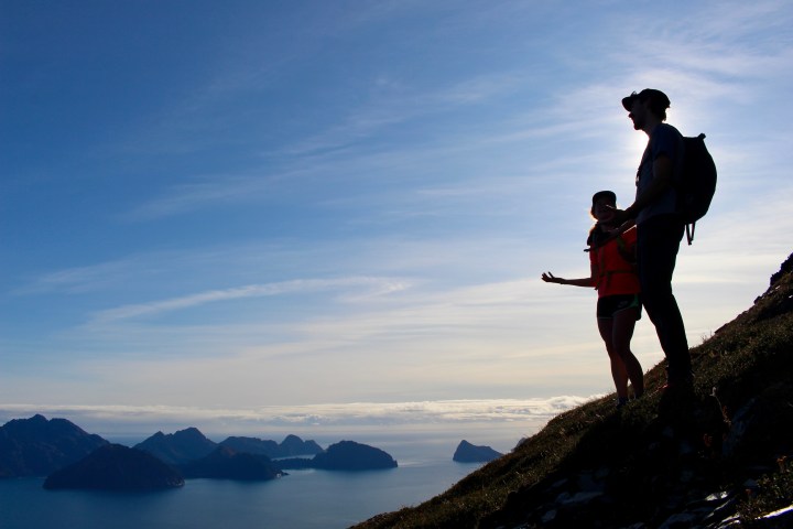 Two people stand on a mountain with a view of the barrier islands and Gulf of Alaska