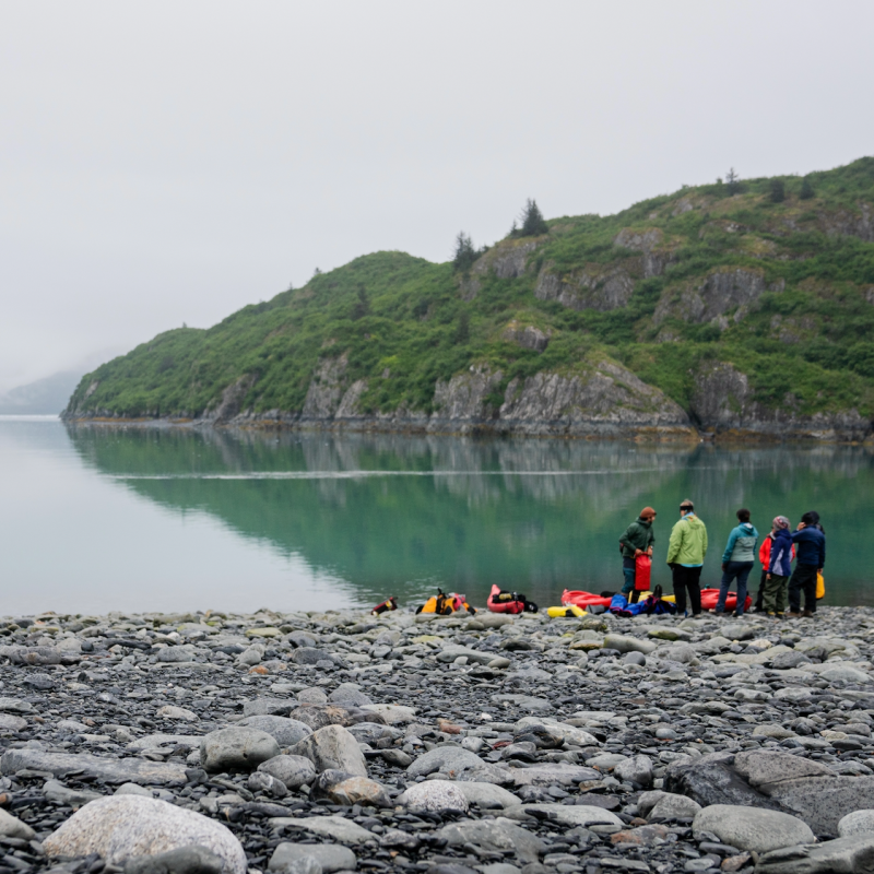 Screen Shot 2022-12-28 at 1.56.20 PM A group of six people stand near red kayaks by the edge of the water